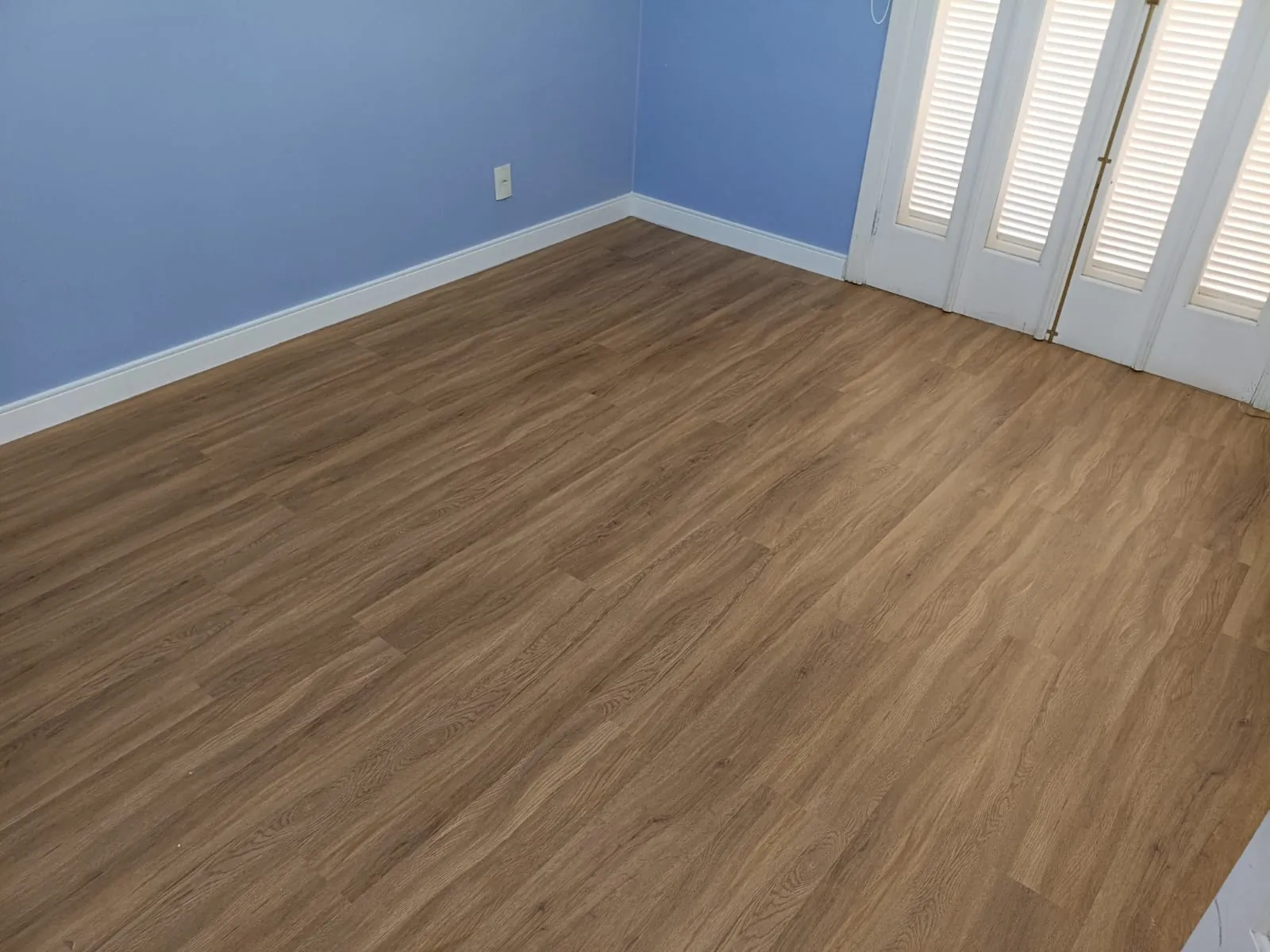 Piso de aspecto amadeirado em quarto com parede azul e rodapé branco.